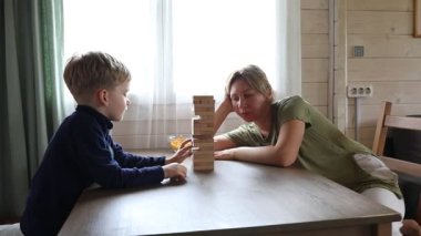 Bir anne ve küçük oğlu evlerindeki bir masada Jenga oynuyorlar. Çocuk, annesi dikkatle izlerken kuleden bir blok çekmek için uzanır..