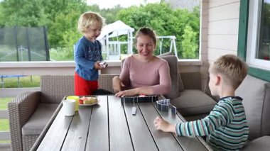 Bir anne ve iki küçük oğlu güneşli bir öğleden sonra teraslarında domino oynuyorlar. Kahkahalar ve gülücükler sırayla fayansları yerleştirip birbirlerine eşlik ederek havayı doldurur.