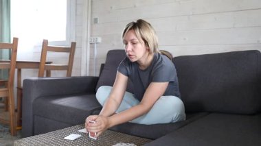 Bir kadın oturma odasındaki sehpanın üzerine iskambil kağıdı serer. Gri bir koltukta oturuyor ve bir kart oyununa hazırlanıyor gibi görünüyor..