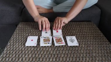 Bir kadın masaya iskambil oynuyor. Her kartı dikkatlice yerleştiriyor, teker teker. Kartlar görünür ve kolayca görülebilir..