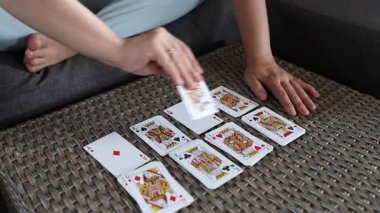 Bir kadın hasır bir bluzla masaya kağıt oynuyor. Kartlar bir çizgi halinde dağılıyor ve kadın onları yerleştirmek için sağ elini kullanıyor. Sahne yakından çekiliyor ve arka plan bulanık..