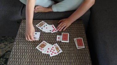 Oturma odasındaki masada kağıt oynayan bir kadın. Kanepede oturuyor ve iskambil oynuyor gibi görünüyor..