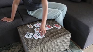 Oturma odasındaki bir kanepede oturan bir kadın önündeki masaya bir deste iskambil kâğıdı serer..