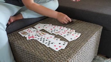 Bir kadın hasır bir masanın üzerine iskambil destesi seriyor. Kartlar vantilatör şeklinde dağıtılmış ve kadın yakınlardaki bir kanepede oturuyor..