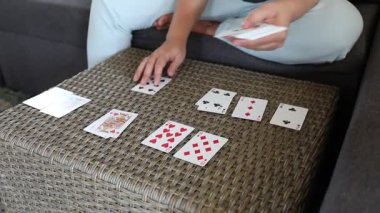 Bir kadın kanepeye oturur ve önünde hasır bir masada kağıt oynar. Kartları sıraya diziyor, sonra da belli bir düzene sokuyor. Olay yeri rahat ve evcil..