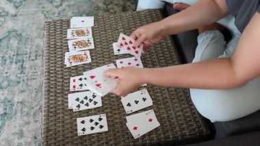 Bir kadın masada oturuyor ve iskambil oynuyor. Gri bir gömlek giyiyor ve bir sandalyede oturuyor. Masa hasırdan yapılmıştır ve dokuma deseni vardır. Kadın kartları sıraya diziyor, ve hepsi yüzükoyun yatıyor..