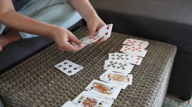 Bu video, bir kadının evdeki bir masada iskambil kağıtlarıyla el ele tutuşmasını gösteriyor. Kanepede oturuyor ve her kartı dikkatlice yerleştiriyor. Kartların yüzlerini gösteriyor..
