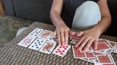 Bir kadın masanın üzerine iskambil oynuyor. O bir kanepede oturuyor ve elinde bir deste kağıt var. Kartları belirli bir düzende düzenliyor..
