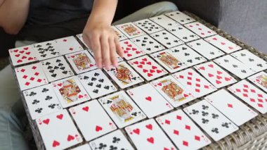 Bir kadın, bir deste iskambil kâğıdını masaya serer ve oyun için hazırlanır. Kartları dikkatlice bir şebeke şeklinde yerleştiriyor, strateji ve şans oyununa hazır..