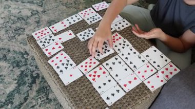 Bu video, hasır masada kağıt oynayan bir kadını gösteriyor. Kartlar belli bir düzende ve o da oyununa odaklanmış durumda..