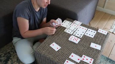 Bir kadın içeride hasır bir masada kart oynuyor. Kartları dikkatlice serer, masanın üzerinde bir desen oluşturur..