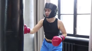 Spor salonunda boks eldiveni ve baş gardiyan takan bir kadın ağır bir torbaya vurarak antrenman yapıyor..