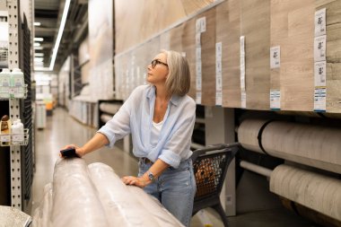 Hareketli bir hipermarkette, bir kadın ev ürünlerini düşünceli bir şekilde kullanır, alışveriş deneyiminde çeşitli bölümlerde bir yansıma ve seçim anı yaratır..