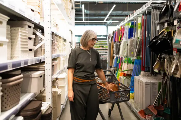 Bir kadın, ev eşyaları, dekor ve bitkileri keşfetmek için aktif olarak bir süpermarketten ürünler seçiyor. Koridorlarda gezinirken gerçek bir ilgi gösteriyor..
