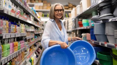 Olgun bir kadın, ev dekorasyonu mağazasında çeşitli ev ürünlerini zevkle inceler. İhtiyacı olan kaliteyi ve uygunluğu değerlendirirken dikkatle kaseleri seçer..
