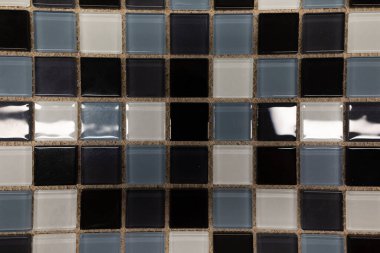 Geometrik desenli mozaik fayanslar bir yüzeyi kaplar ve mavi, siyah ve gri tonlarını gösterir. Düzenleme, görsel olarak çarpıcı bir etki yaratan doku ve renklerin bir karışımını vurgular..