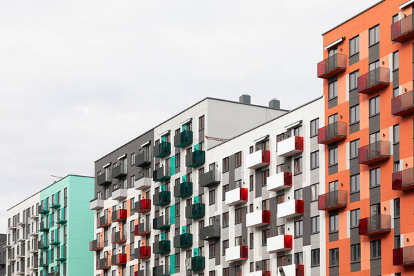 A cluster of contemporary high-rise apartment buildings showcases vibrant facades and balconies in a bustling residential area under cloudy skies. Residents enjoy urban living amenities.