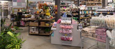 Müşteriler çeşitli ev onarımı, dekorasyon ve bahçe ürünleriyle dolu iyi organize edilmiş bir hırdavat dükkanına göz atıyorlar. Parlak yerleşim çeşitli sunumları vurguluyor.