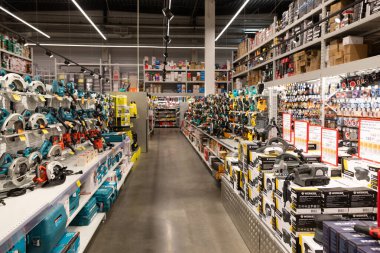 Müşteriler, ev onarımı ve iyileştirmeye uygun çeşitli araç gereçler ve ekipmanlarla çevrili iyi organize edilmiş bir hırdavatçı reyonuna göz atıyorlar. Parlak ve ferah.