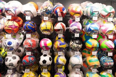 Futbol ve voleybol da dahil olmak üzere çeşitli spor topları bir hırdavatçıdaki raflarda düzenli olarak düzenlenmektedir. Müşteriler yoğun bir öğleden sonra renkli seçimleri gözden geçirirler.
