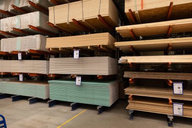 Kereste ve inşaat malzemeleri bir hırdavatçıdaki raflarda düzenlenir ve ev onarımı için seçenekler sunulur. Müşteriler malzemelerin çeşitli boyut ve renklerine bakabilirler.