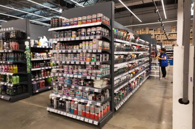 Müşteriler, öğleden sonra yoğun bir alışveriş zamanında, iyi organize edilmiş bir hırdavatçıda çeşitli tamir malzemeleri ve aletlerle dolu koridorlara göz atıyorlar..