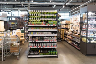 Tamir malzemeleri ve aletlerle dolu raflar iyi aydınlatılmış bir hırdavatçıda düzgünce düzenlenirken, müşteriler gün içinde ev ihtiyaçlarını gidermek için koridorları gözden geçiriyorlar..