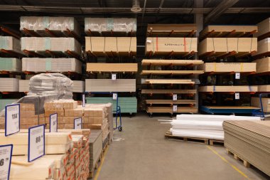 Çeşitli inşaat malzemeleri ve aletleri bir tamir mağazası koridorunda düzgünce düzenlenir. Raflar ahşap, tahta ve malzemelerle dolu. Müşteri projeleri için hazırlar..