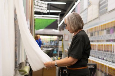 Bir müşteri tekstil dükkanında farklı kumaş örneklerini inceler. Renkli cıvatalarla çevrelenmiş halde, düşünceli bir şekilde projesi için seçenekler seçiyor, yaratıcılığını ve ilhamını gösteriyor..