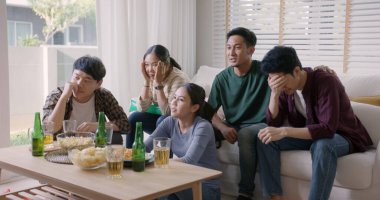 Bir grup Asyalı genç yetişkin erkek ve kadın çığlık atıyor. Heyecanlı bir şekilde kanepede oturup FIFA dünya kupası izliyorlar. TV 'de canlı yayında..