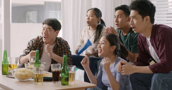 Group of young adult friend man and woman asia people sit at sofa couch joy chanting party fun game FIFA world cup live TV at home eat snack bowl drink beer bottle glass jump mad happy win exult face.