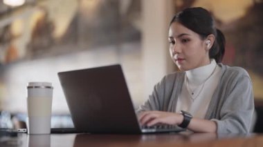 Genç yetişkin Gen Z kadın Asyalılar kafelerde mutlu bir hibrid olarak çalışıp laptopta cevap yazıyorlar sosyal medyada SEO haberleri okuyorlar. Zeki Asyalı kadın hisse senedi tüccarı kendini yenileme becerisi
