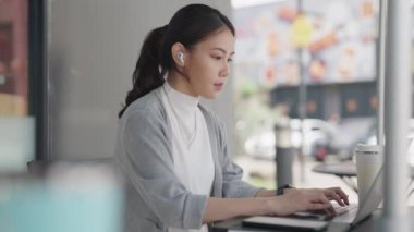 Genç yetişkin Gen Z kadın Asyalılar kafelerde mutlu bir hibrid olarak çalışıp laptopta cevap yazıyorlar sosyal medyada SEO haberleri okuyorlar. Zeki Asyalı kadın hisse senedi tüccarı kendini yenileme becerisi
