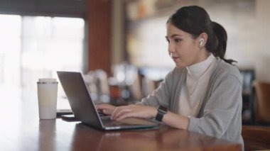 Genç yetişkin Gen Z kadın Asyalılar kafelerde mutlu bir hibrid olarak çalışıp laptopta cevap yazıyorlar sosyal medyada SEO haberleri okuyorlar. Zeki Asyalı kadın hisse senedi tüccarı kendini yenileme becerisi
