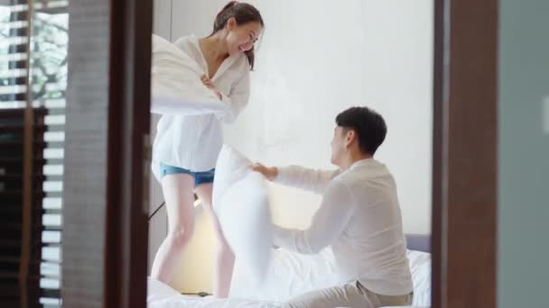 年轻夫妇两个亚洲人放松快乐笑着笑着在床上玩枕头大战安乐窝亚洲情人刚结婚的男人在家庭生活中开始快乐甜蜜的时刻 — 图库视频影像
