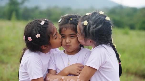3人の可愛い子どもアジア系の姉妹は 楽しい時間親友を持っているカメラの笑顔の楽しさを頬抱っこ抱擁見てキス 多様な肌の弟若いです人々小さな子供女の子愛信頼リラックス幸せな甘い瞬間 — ストック動画
