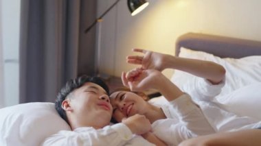 Top view young couple asia people lying down talk on bed relax smile hold hands look at ring on finger. Sweet happy lover asian man woman fall in true love new family life begin just married moment.