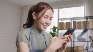 Go green SME owner reply chat comment online talk or set up chatbot on phone. Young seller asia woman typing mobile at home office easy selling CRM platform for eco friendly shop retail net zero store