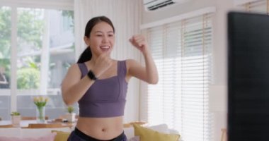 Young active asia woman laugh smile cool down finish body cardio on online gym plan on TV at cozy home. Self love happy joy fun life balance people health care with sport smart watch fitness tracker.