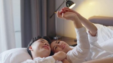 Top view young couple asia people lying down talk on bed relax smile hold hands look at ring on finger. Sweet happy lover asian man woman fall in true love new family life begin just married moment.