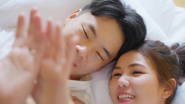 トップ表示若いカップルアジアの人々のベッドの上で話を横に笑顔をリラックスホールド手を指にリングを見てください 甘いです幸せな恋人アジア人男性女性秋で真の愛新しい家族生活開始ちょうど結婚式の瞬間 — ストック動画