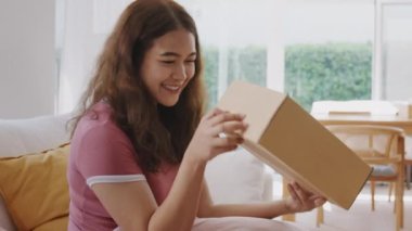 Asyalı genç bir kadın gülümsüyor. Sevgi koli kutusuna sarılıyor. Mallar karton kutuya sarılıyor. Omni kanalı hediye siparişinin keyfini sürün. Perakende mağazasından postayla alın. Hızlı kurye gönderme servisi..