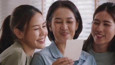 Recall the past life memories Happy time Mother's day grown up kid child joy fun look at old retro photo album with mature mum. Asia adult people middle age mom smile enjoy relax sitting at home sofa.