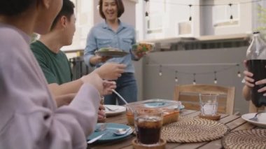Mom enjoy cooking for family day dining at dine table cozy patio front yard home. Mum passing food serving drink to group four asia people young adult man woman friend fun joy relax warm picnic eating