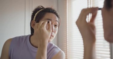Eşcinsel eşcinsel adam ikili olmayan güzellik blogcusu makyaj sanatçısı evde kadın kıyafeti giyip yüz bakımı makyaj fırçası sürüyor. Gerçek Asya LGBT genç adam mutlu yetişkin insanlar rahatlayın ayna gururuna bakarak gülümseyin.