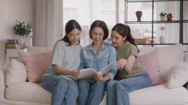Buy mediclaim health care life insure for older mum. Young adult woman asia people grown up child give gift to middle aged mom reading protect cover saving plan paper smile laugh sitting at sofa home.