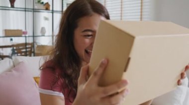 Asyalı genç bir kadın gülümsüyor. Sevgi koli kutusuna sarılıyor. Mallar karton kutuya sarılıyor. Omni kanalı hediye siparişinin keyfini sürün. Perakende mağazasından postayla alın. Hızlı kurye gönderme servisi..