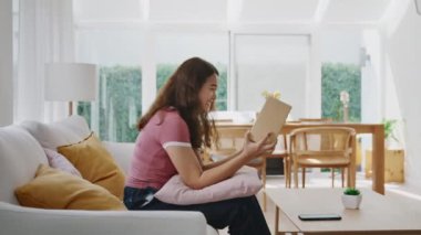 Asyalı genç bir kadın gülümsüyor. Sevgi koli kutusuna sarılıyor. Mallar karton kutuya sarılıyor. Omni kanalı hediye siparişinin keyfini sürün. Perakende mağazasından postayla alın. Hızlı kurye gönderme servisi..