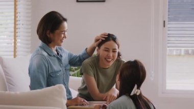 Middle aged mom smile look at two grown up kid child relax hug cuddle stroking with love care warm time. Asia people woman adult older mum parent sitting at home sofa sweet trust moment happy life.