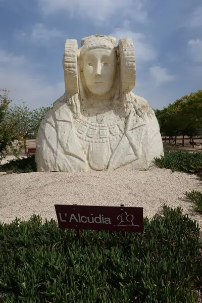 stock image Ilici - La Alcudia, archaeological site. Elche, Alicante, Spain, June 19, 2024: Large bust of The Lady of Elche in a road in Ilici - La Alcudia, archaeological site. Elche, Alicante, Spain